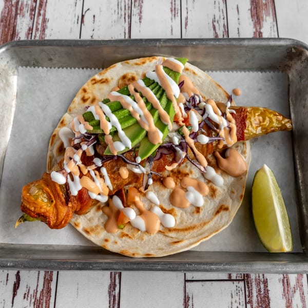 Calle Taco's Mexican taco with avocado, red cabbage, and sauces, served with a lime wedge.