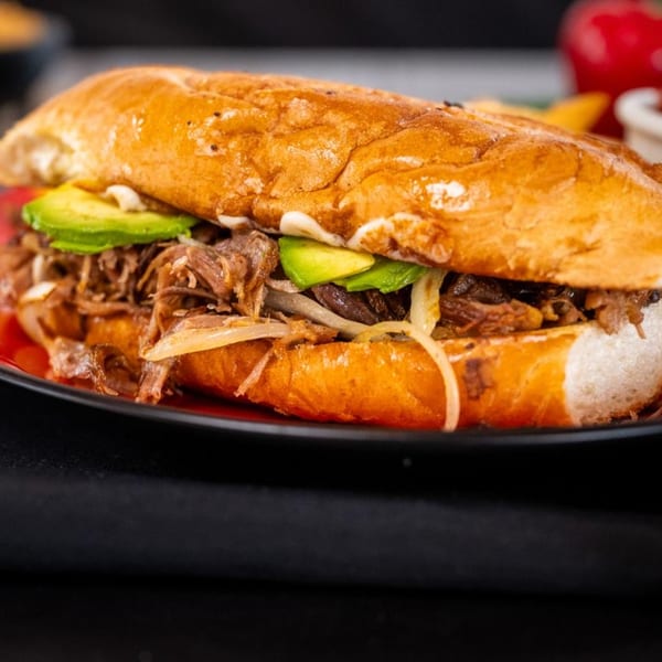 Calle Taco's Mexican torta sandwich, filled with shredded meat, avocado, and onions on a red plate.